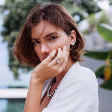 Woman with short brown hair wearing a white top and diamond ring outdoors.